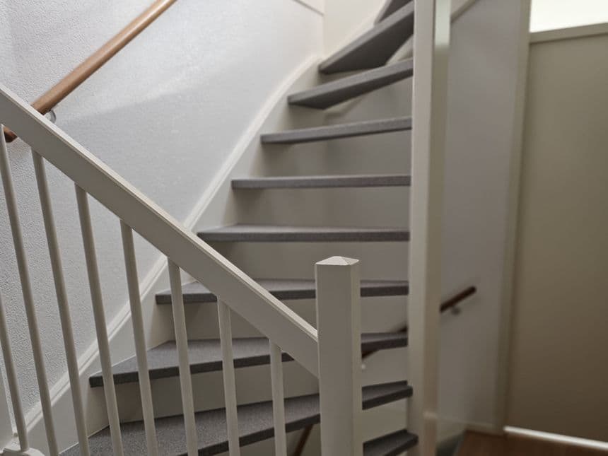 Beginsituatie trap voor renovatie — geschilderde houten trap met grijze treden en witte spijlen
