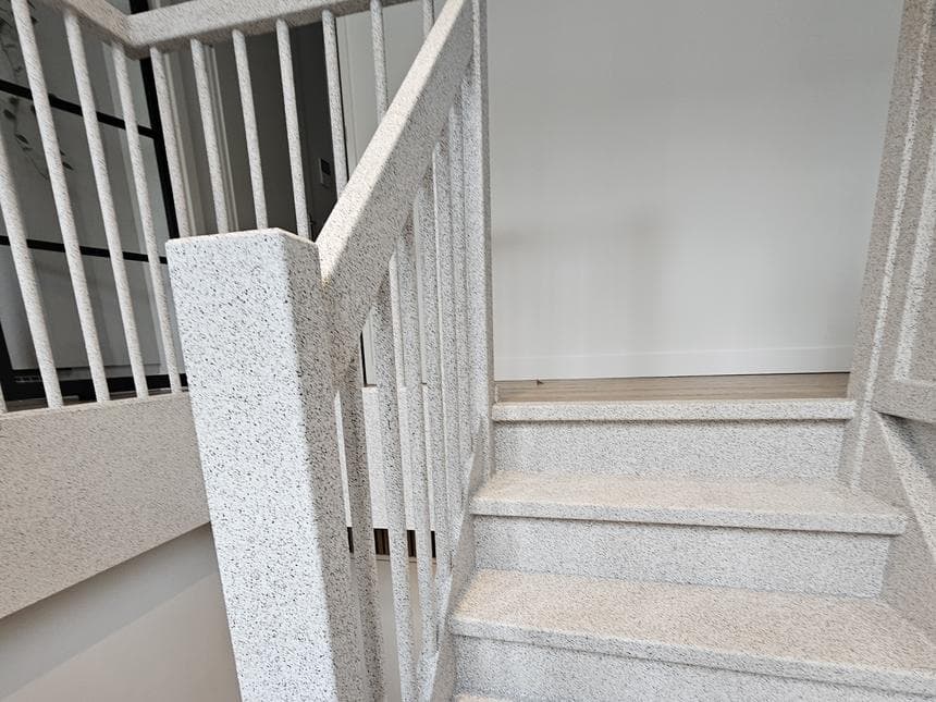 Eindresultaat uitgevoerd door Creastairs — volledige trapafwerking inclusief zijwangen, palen en treden in licht Stone gemelieerd composiet